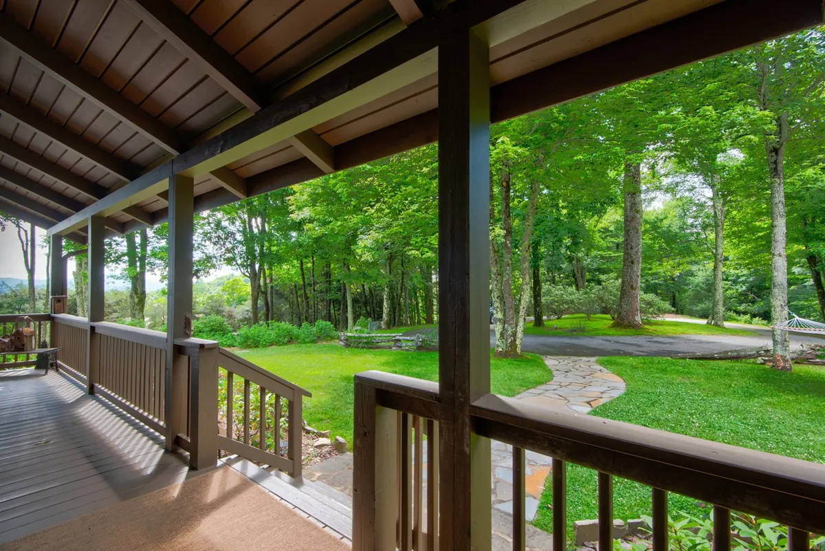 A wooden deck with cozy railings overlooks a lush green landscape, with a stone walkway leading into the woods. The area is perfect for morning coffee, leisurely walks, or simply enjoying the serene surroundings.