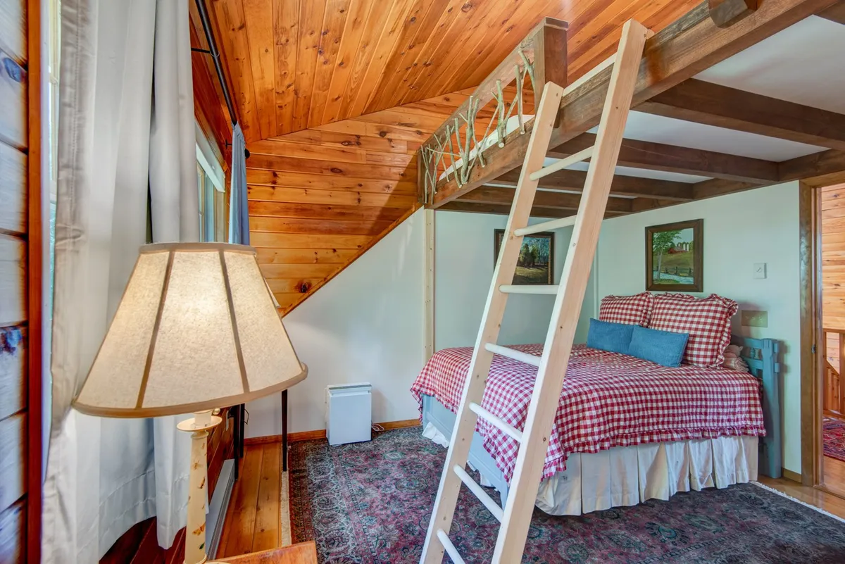 A playful and inviting bedroom with a twin-over-queen bunk bed, checkered bedding, sturdy wooden ladder, and a lamp providing a warm glow. The design is ideal for families or groups, offering both comfort and a sense of fun.