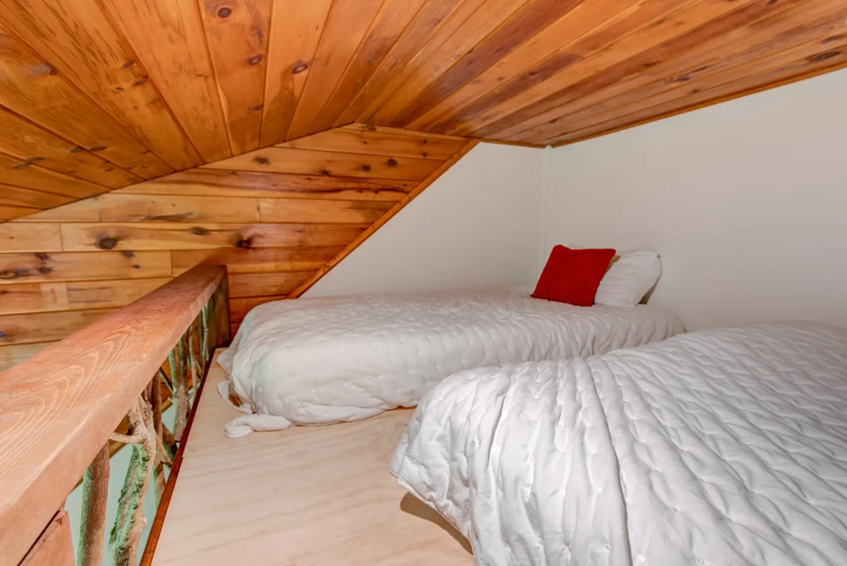 A tranquil loft space with a wooden ceiling and two beds adorned with red pillows. The soft lighting and intimate arrangement evoke a sense of peaceful retreat, making it suitable for both rest and quiet play.