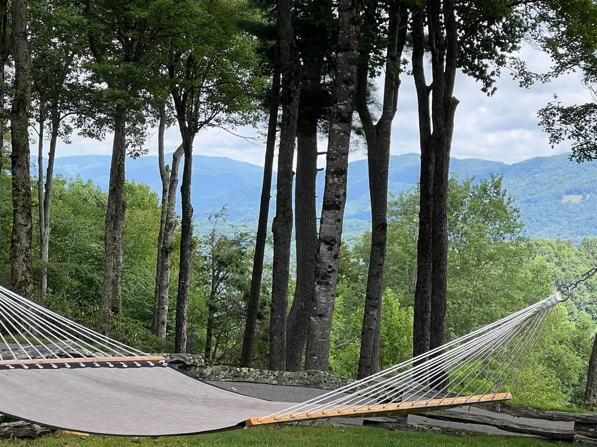 This image features a hammock strung between trees with a clear mountain view in the background. The surrounding foliage provides shade and a sense of seclusion, suggesting a peaceful retreat. The hammock invites relaxation, whether for reading, napping, or stargazing at night.
