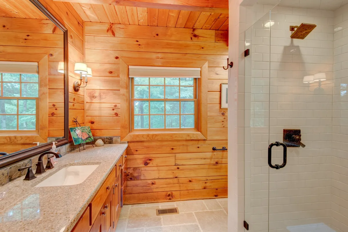 A spacious bathroom with rich wooden cabinetry, a sleek granite countertop, and a glass-enclosed shower. Large windows bathe the room in natural light, creating a serene environment ideal for unwinding after a day of adventure.