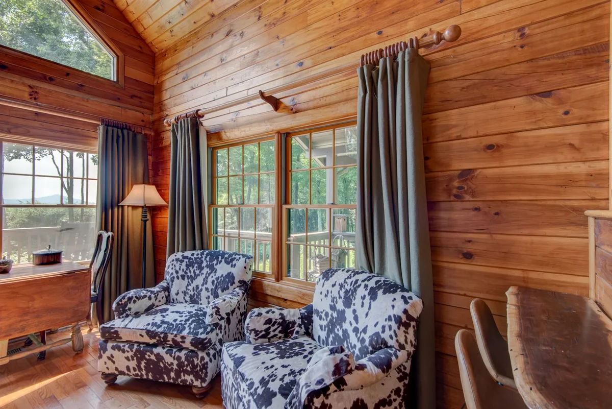 A welcoming interior corner featuring cow print chairs, wooden beams, and large windows. The setting feels intimate and cozy, ideal for reading or quiet reflection, and benefits from abundant natural light.